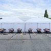 Two large white pop up tents with sidewalls, folding tables, and black chairs set up in a Burnaby parking lot with boxed lunches on each table