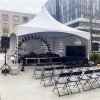 20x20 white marquee tent with stage, balloon arch, TV screen, and rows of black folding chairs set up on a concrete plaza for an outdoor corporate event in Surrey, BC
