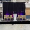 12x16 black stage with podium and chairs in front of black pipe and drape with purple uplighting at Seaforth Armoury in Vancouver, BC