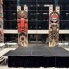 8x12 black portable stage with stairs and black skirting set up inside the Museum of Anthropology at UBC in front of large Indigenous carved house posts