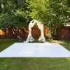 White dance floor on backyard lawn in front of a draped wedding arch with floral arrangements.